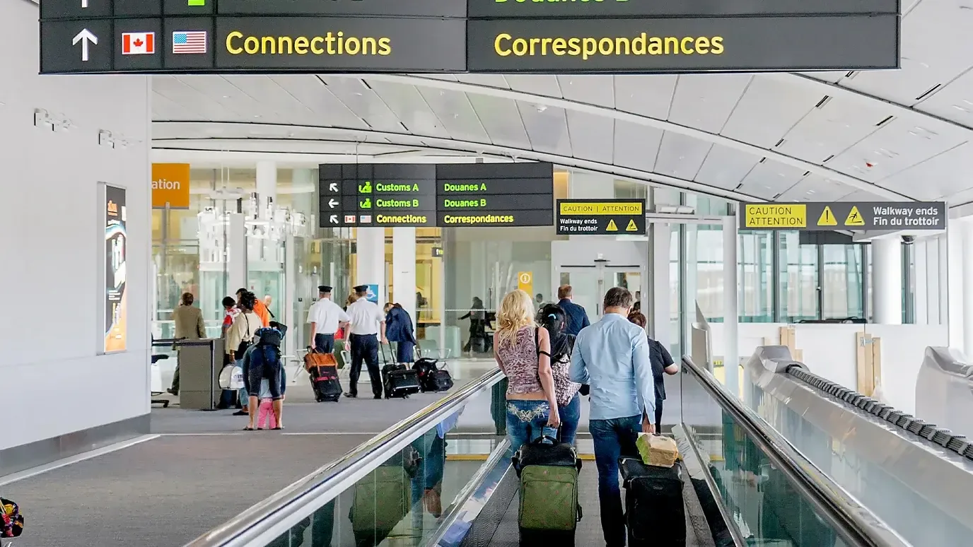 Travelers with suitcases on a moving walkway in a Canadian airport, under bilingual Connections signs
