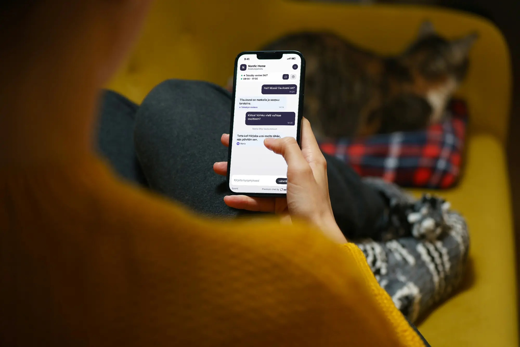 A customer chats with a shop on a phone. The Askly chat on the screen shows a question in Finnish, the AI's answer and Maria from the team taking over.
