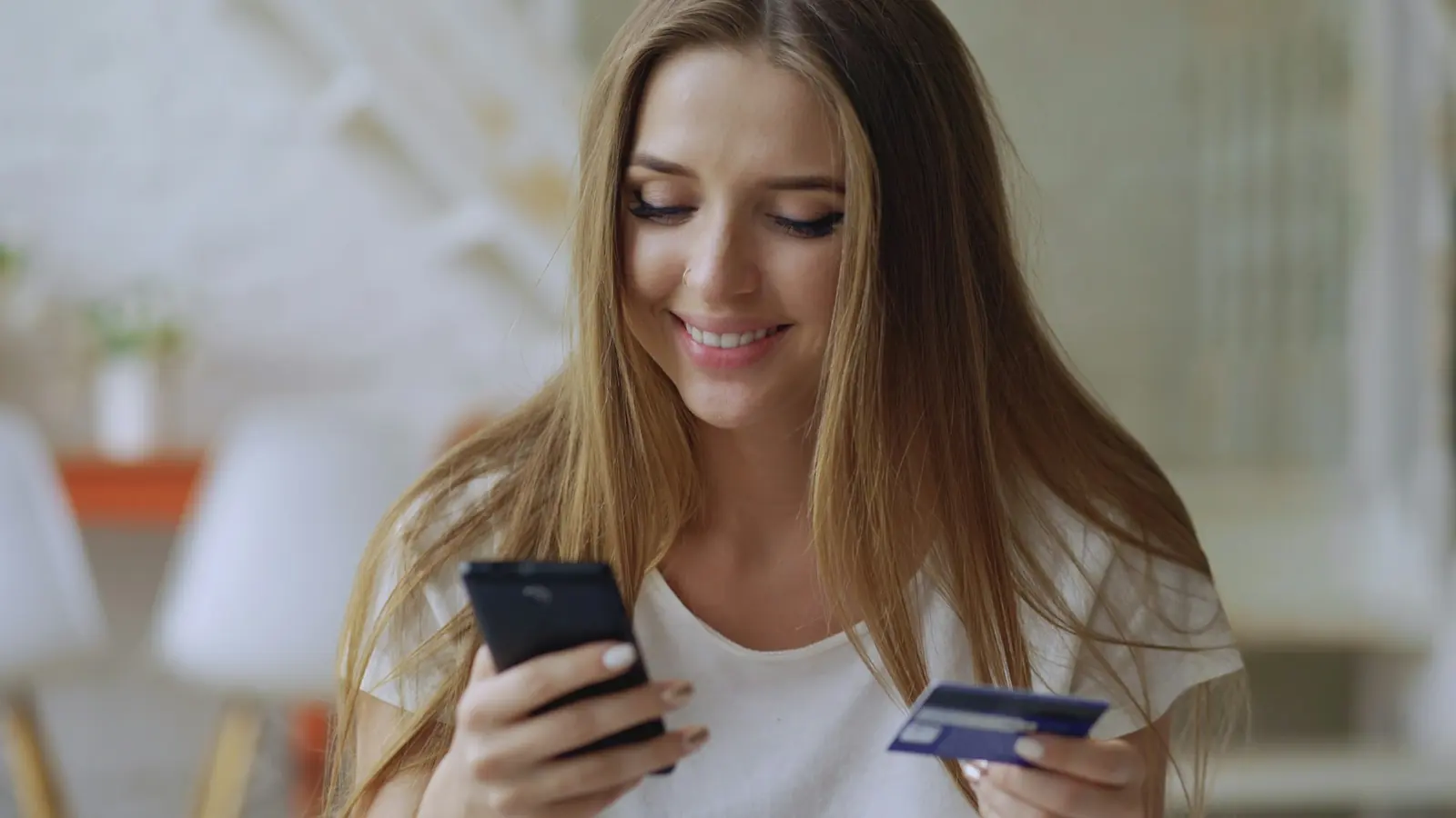 A smiling customer shops online with a phone and a bank card.